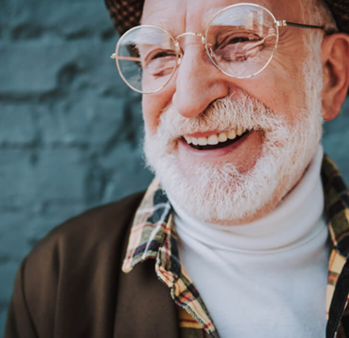 Bearded man with glasses smiling in front of wall