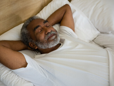 Senior man lying in bed and sleeping with hands behind head