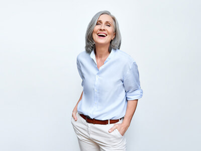 Senior woman with hands in pockets laughing