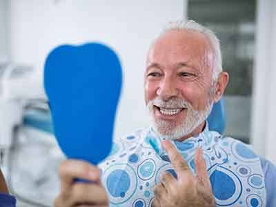 a smiling man looking at his teeth in a mirror