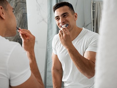 Man smiling at reflection while brushing teeth
